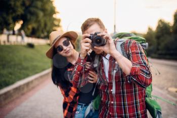 Hikers with backpacks go sightseeing in tourist town and makes photo for memory. Summer hiking. Hike adventure of young man and woman