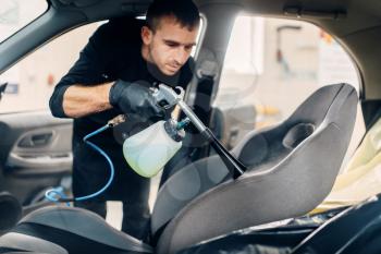 Professional dry cleaning of car seats. Carwash service, male worker using spray