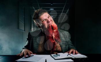 Crazy businessman with a piece of raw meat in his mouth against stacks of paper in office. Mad businessperson works with documents, bad emotion, stressed manager
