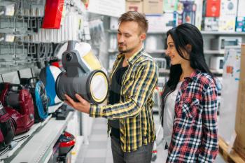 Young couple choosing vacuum cleaner in supermarket. Male and female customers on family shopping. Man and woman purchasing goods for the house