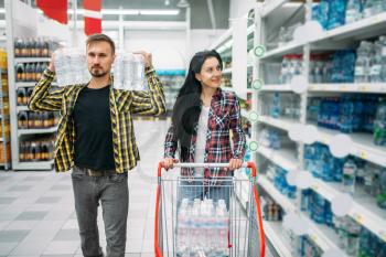 Couple buying mineral water in supermarket. Male and female customers on family shopping. Man and woman purchasing beverages