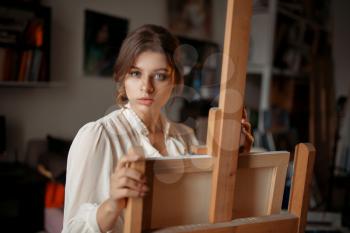 Thoughtful female artist at the easel in studio. Creative paint, painter drawing artwork, workshop interior on background
