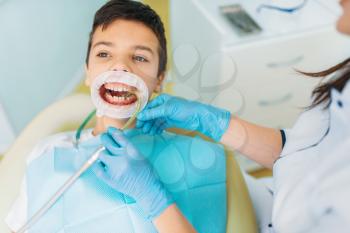 Little boy in a dental cabinet, caries removal procedure, pediatric dentistry. Female dentist works with child
