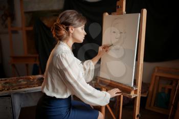 Female painter in studio, pencil sketch on easel. Creative paint, woman drawing portrait, workshop interior on background