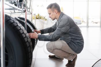 Man choosing tyres for new car in showroom. Male customer buying vehicle in dealership, automobile sale, auto purchase