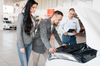 Manager shows the couple a new car in showroom. Male and female customers looks vehicle in dealership, automobile sale, auto purchase