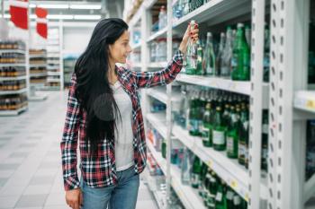 Young woman buying mineral water in supermarket. Female customer on  shopping in hypermarket, department of beverages