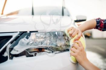 Female person with sponge cleans vehicle headlight, car wash. Young woman on self-service automobile washing. Outdoor carwash at summer day 