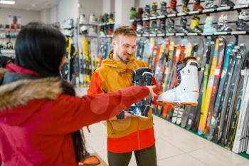 Couple at the showcase choosing ski or snowboarding boots, shopping in sports shop. Winter season extreme lifestyle, active leisure store, customers buying skiing equipment