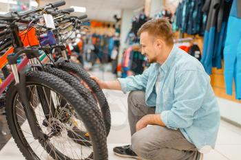 Man checks bicycle tyre, shopping in sports shop. Summer season extreme lifestyle, active leisure store, customer buying cycle equipment