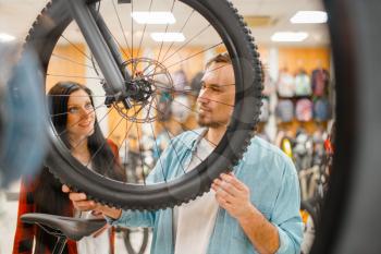 Man checks bicycle disk breaks, shopping in sports shop. Summer season extreme lifestyle, active leisure store, customers buying cycle, couple choosing bikes
