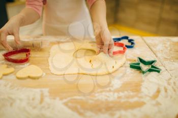 Little girl cook in apron makes cookies in the shape of a heart on the kitchen. Kid cooking pastry, child chef preparing cake