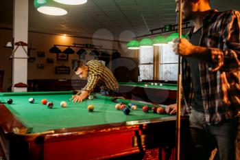 Two male billiard players with cues poses at the table with colorful balls, poolroom. Men plays american pool game in the sport bar