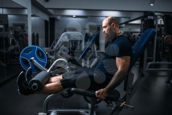 Muscular athlete trains legs on exercise machine, training in gym. Bearded man on workout in sport club, healthy lifestyle