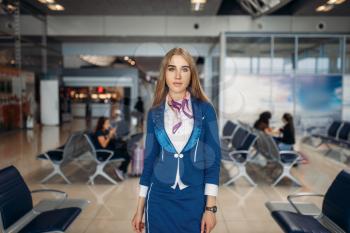 Stewardess poses in airport waiting area. Air hostess in departure zone, flight attendant in terminal, aviatransportations job