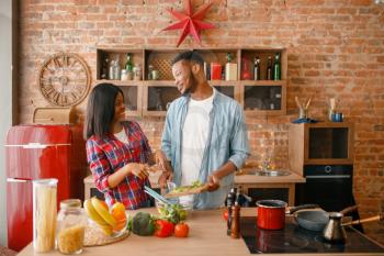 Playful black couple cooking romantic dinner on the kitchen. African family preparing vegetable salad at home. Healthy vegetarian lifestyle