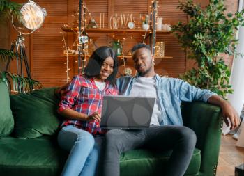 Black couple sitting on sofa and looking on laptop at home. Happy african love couple leisures in their house