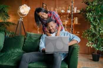 Black couple with laptop having fun on sofa at home. Happy african love couple leisures in their house, cheerful family relaxing at home