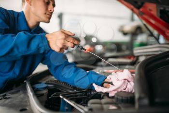 Male technician checks car engine oil level with dipstick. Auto-service, vehicle maintenance, repairman with tools