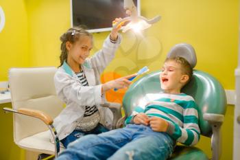 Little girl in uniform playing dentist doctor, playroom. Kids plays medicine worker in imaginary hospital, stomatologist profession learning, childish dream