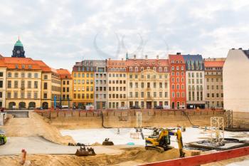 Construction site in the middle of the old european city. Excavator works with sand pile, cityscape on background, building engineering