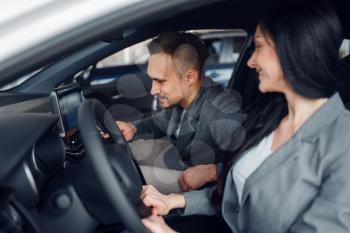 Happy couple buying new car in showroom, woman behind the wheel. Male and female customers choosing vehicle in dealership, automobile sale