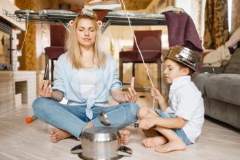 Young housewife and kid sitting in yoga pose at the ironing board. Woman with child leisures at home together. Female person with son having fun in their house