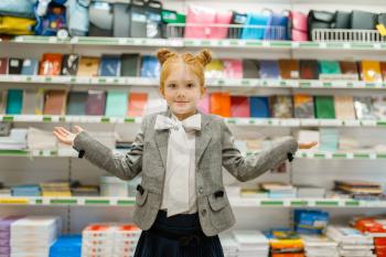 Little school girl at the shelf in stationery store, front view. Female child buying office supplies in shop, schoolchild in supermarket