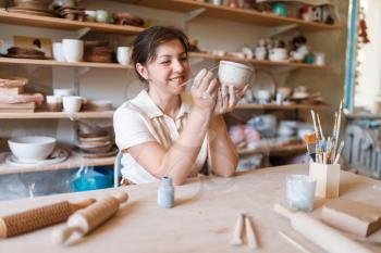 Female master paints a pot, pottery workshop. Woman molding a bowl. Handmade ceramic art, tableware from clay