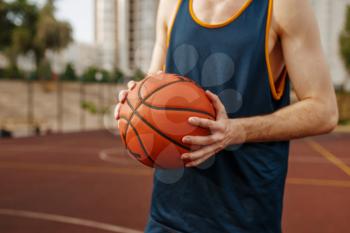 Basketball player aiming for the throw on outdoor court. Male athlete in sportswear holds ball on streetball training