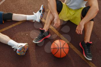 Two basketball players sitting on the ground on outdoor court. Male athletes in sportswear after streetball training
