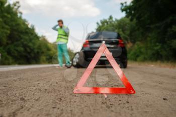 Emergency stop sign, car breakdown, man calling for tow truck on background. Broken automobile or repairing of flat tyre on vehicle, trouble with punctured auto tire on highway
