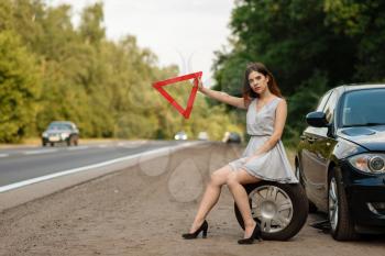 Car breakdown, young woman with emergency stop sign vote on the road, flat tyre. Broken automobile or problem with vehicle, trouble with punctured auto tire on highway