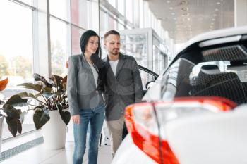 Happy couple buying new car in showroom. Male and female customers choosing vehicle in dealership, automobile sale, auto purchase