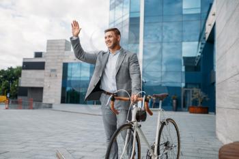 Businessman cyclist in suit in downtown, glass building on background. Business person riding on eco transport on city street