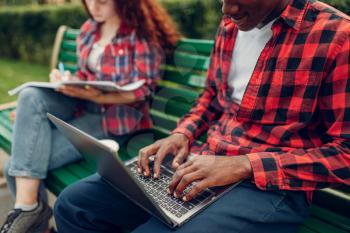 Two students studying on the bench in summer park. Male and female white teenagers relax outdoors