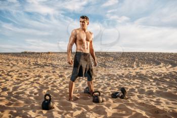 Male athlete doing exercises with dumbbells in desert at sunny day. Strong motivation in sport, strength outdoor training