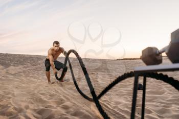 Male athlete doing exercise with battle ropes in desert at sunny day. Strong motivation in sport, strength outdoor training
