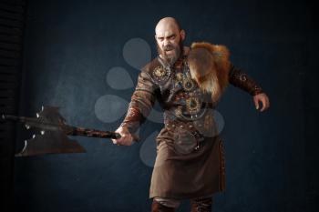 Angry viking with axe dressed in traditional nordic clothes, barbarian image. Ancient warrior.