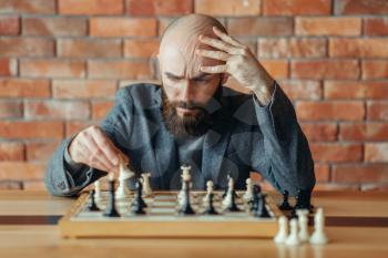 Male chess player understood that he lost, checkmate. Chessplayer at board, front view, intellectual tournament indoors. Chessboard on wooden table, strategy game