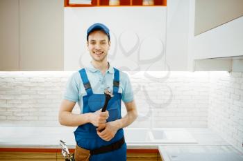 Male plumber in uniform fixing faucet in the kitchen. Handyman with toolbag repair sink, sanitary equipment service at home