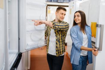 Young family couple choosing refrigerator in electronics store. Man and woman buying home electrical appliances in market