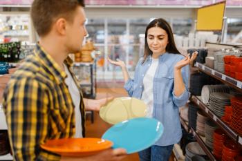 Young couple choosing plates in houseware store. Man and woman buying home goods in market, family in kitchenware supply shop