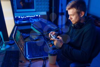 Male gamer in headphones holds joystick and playing videogame on console or desktop PC, gaming lifestyle, cybersport. Computer games player in his room with neon light, streamer