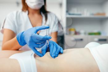 Cosmetician in gloves gives botox injection in the stomach to female patient on treatment table. Rejuvenation procedure in beautician salon. Doctor and woman, cosmetic surgery against wrinkles