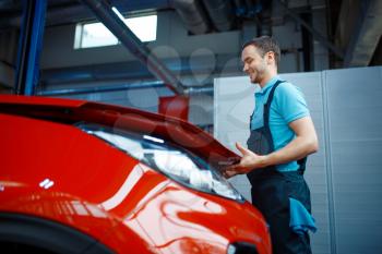 Worker in uniform opens vehicle hood, car service station. Automobile checking and inspection, professional diagnostics and repair