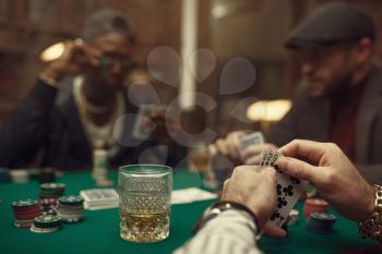 Two poker players with cards sitting at gaming table with green cloth in casino. Games of chance addiction, risk, gambling house. Men leisures with whiskey and cigars