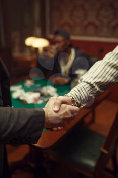 Male poker players shake hands in casino. Games of chance addiction, risk, gambling house. Men leisures with whiskey and cigars