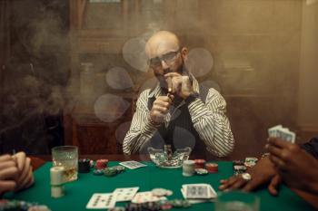 Bearded poker player with cigar, casino. Games of chance addiction. Man leisures in gambling house. Cards, chips and whiskey on gaming table