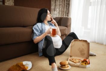 Pregnant woman with belly smoking and drinks beer at home. Pregnancy and bad habits, unhealthy lifestyle in prenatal period. Ugly expectant mom, health damage, alcoholism